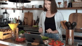 Pretty young woman cooking dietary meal from fresh vegetables browse online recipe on tablet. Caucasian lady modern day housewife enjoy culinary at home in modern kitchen. 4k footage