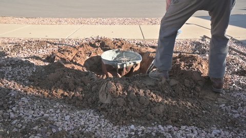 Man shoveling heavy clay sand to dig out an underground trash can, slow motion.