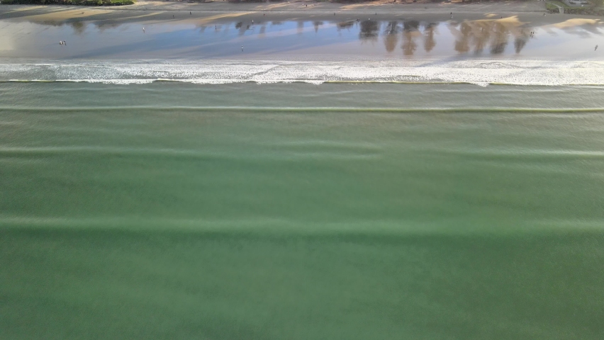 Drone pan up of relaxing waves along the beach at sunset