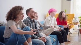 Attractive Men Resting at Home playing Video Games at Home and Winning. Group of Male Friends having a Night Party sitting on the couch with Snacks and Drinks. Playing Computer Games using Controllers
