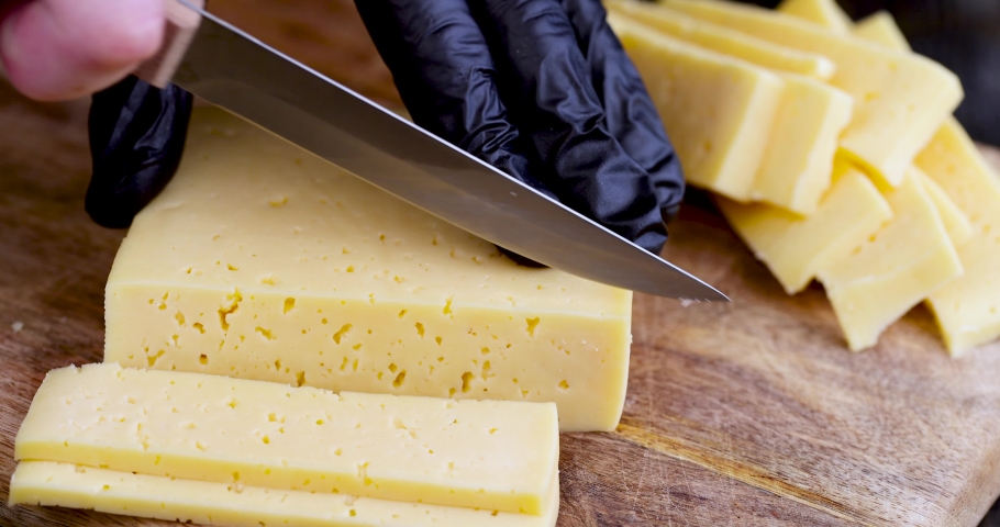 Slicing ripe delicious cow's milk cheese, yellow hard cheese on a cutting board during slicing | Shutterstock HD Video #1091114139