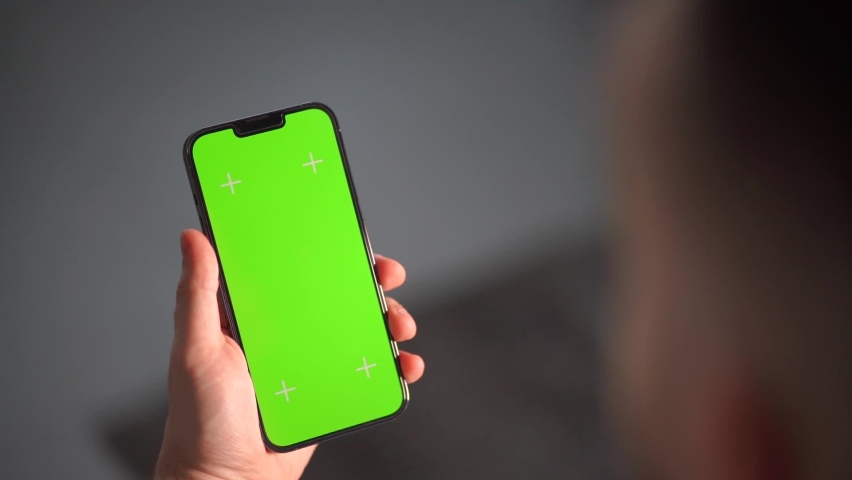 A man's hand is holding a smartphone with the vertical screen visible. guy hand holding a mobile phone with a green screen for keying and tracking Royalty-Free Stock Footage #1091117717