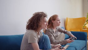 Lesbian LGBTQ women couple play video game at home. Young Asia lady using wireless controller having funny happy moment together on sofa in living room. They have great and fun time celebrate holiday.