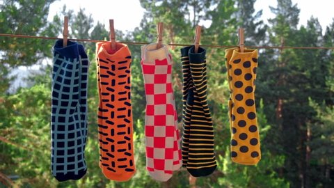 colorful bright men's socks with different patterns are dried on the balcony on a rope in pairs, attached with wooden clothespins. against the background of the trees. close-up. slow motion.