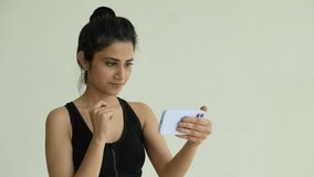 A Indian young fitness woman holding smartphone relaxing after workout at home. Smiling Indian female using video call phone calling while exercise.