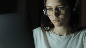 Teenage girl with glasses looks at the monitor, plays a game, reads, studies late at night