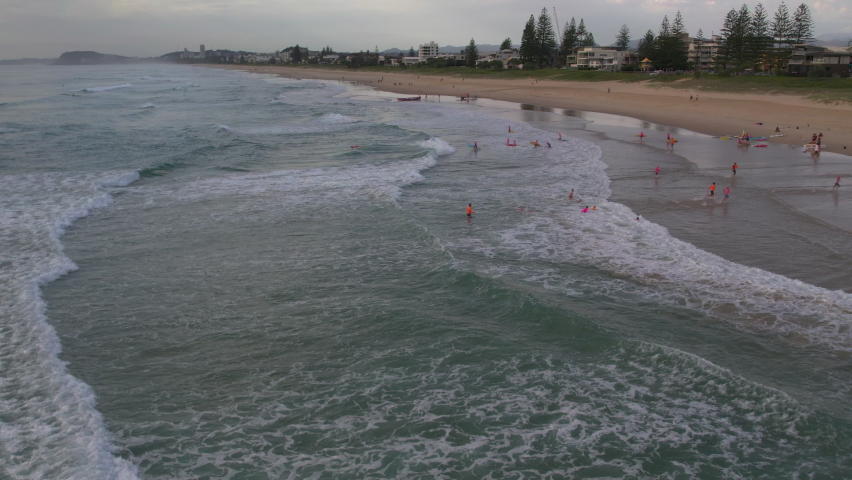 Aerial view of a group of Nippers running from the ocean during a morning training session with water safety watching on at Mermaid Beach Gold Coast QLD Australia