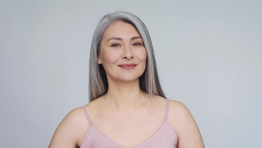Portrait of gorgeous happy middle aged mature asian woman, senior older 50 year lady looking at camera touching her face isolated on white. Ads of lifting anti wrinkle skin care treatment. Royalty-Free Stock Footage #1091130299