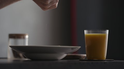 Grinding fresh spices on pasta in plate with glass of orange juice on countertop