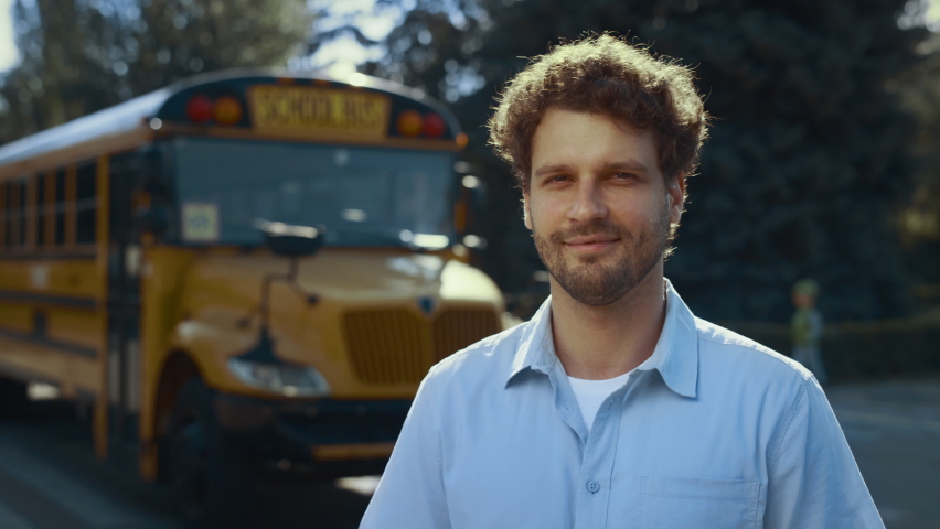 Smiling man driver posing near yellow academic vehicle alone close up. Joyful professional schoolbus operator wearing uniform looking camera. Curly bearded guy standing at school bus waiting pupils. Royalty-Free Stock Footage #1091137523