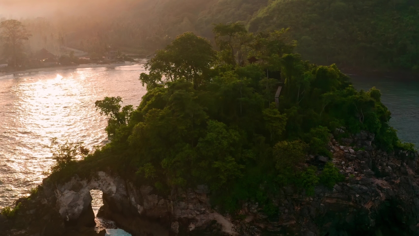 Scenery coastline tropical island with beautiful lagoon on background foggy landscape with mountain in fog in the rays of the rising sun. 4K Aerial view