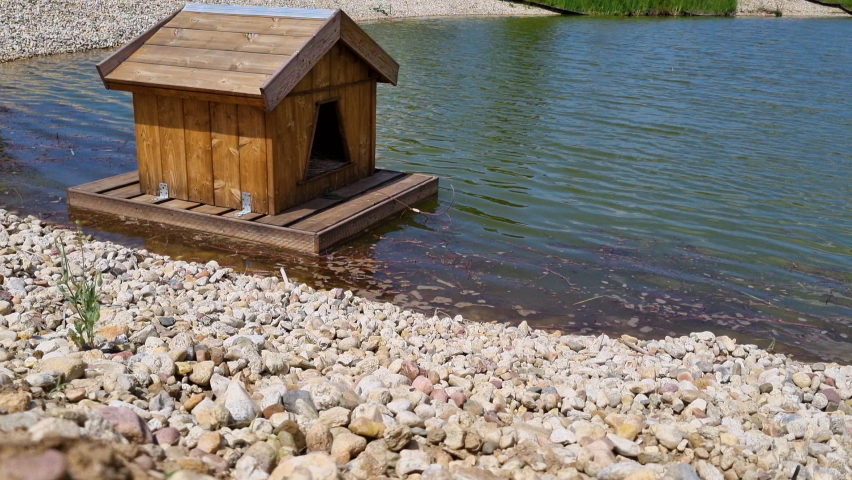 A small wooden duck house floats on the surface of the lake.