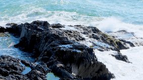 Sea waves hit the rocks. Rocky seashore on a day. Sea waters. Handheld video.