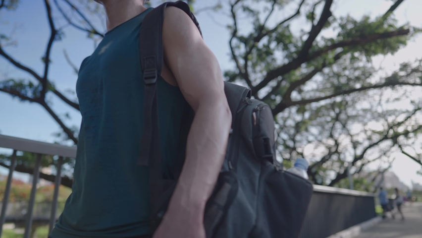 Handsome man carry on the backpack to his shoulder get ready to move, active lifestyle Asian good looking fit male going to the gym walking under trees on good clear weather sunny day, life balanced Royalty-Free Stock Footage #1091147553
