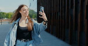 Portrait of young beautiful woman blogger in city holds phone taking on mobile camera shoots video for vlog.