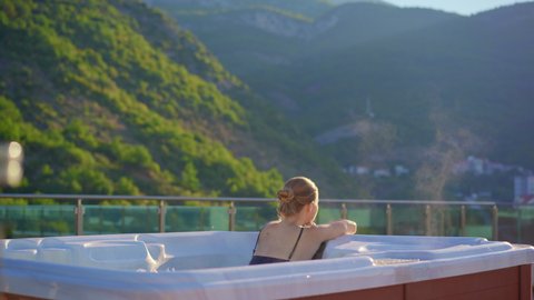 A young woman relaxes in the hot tub on a rooftop with a view on mountains
