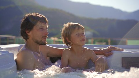 A young man and his son relaxing in the hot tub on a rooftop with a view on mountains