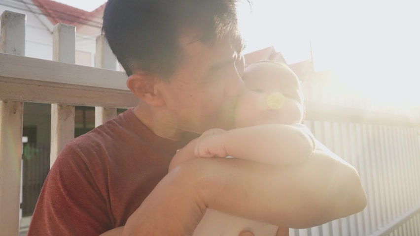 Happy Warm Asian Old Man and Baby Kid in Domestic Comfort. Wrinkled Skin of Grandfather or Black dyed Haired Aged Parent in Casual Summer Day Light. Gentle Embrace and Smile of 60s Retired Grandparent Royalty-Free Stock Footage #1091149883