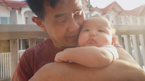 Happy Warm Asian Old Man and Baby Kid in Domestic Comfort. Wrinkled Skin of Grandfather or Black dyed Haired Aged Parent in Casual Summer Day Light. Gentle Embrace and Smile of 60s Retired Grandparent: stockvideo