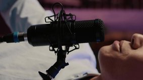 Vertical video: Male vlogger using microhpone to record podcast episode, talking to listeners and audience at studio station with professional equipment. Creating content for social media channel