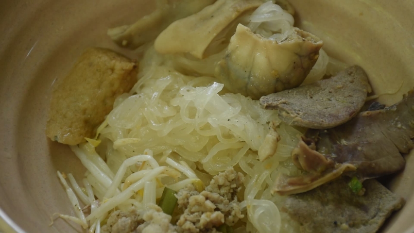 hand squeezing lemon to boiled dry thin rice noodles with entrails and fish line on bowl