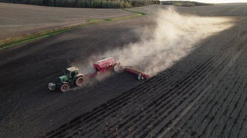 Aerial view of a moving tractor with a harrow system plowing the ground in a farmer's field, raising clouds of dust. Spring agricultural work before sowing corn. Planting and harvesting the first crop