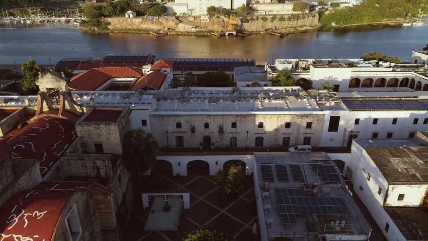 Architectural monuments of the old city on the banks of the river. The capital of the Dominican Republic in the evening rays of the sun. Nature and city life. Aerial view of Santo Domingo at dusk.
