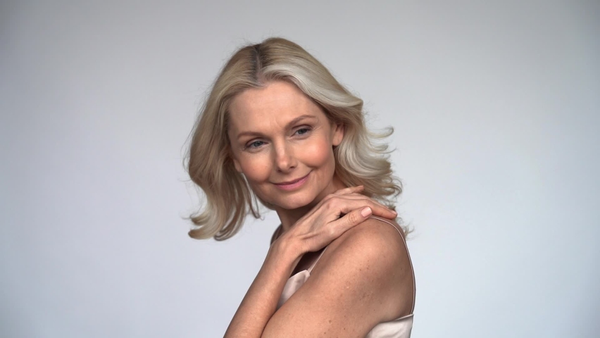 Attractive gorgeous mature older woman looking at camera isolated on white background advertising skincare and hair care treatment. Mid age tightening face skin care rejuvenation cosmetics concept Royalty-Free Stock Footage #1091158689