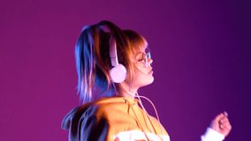 Gen z teen girl model wear headphones listening dj pop music playlist dancing on purple violet neon light color studio background. Stylish 20s hipster fashion woman in hoodie sunglasses at cool party. - Powered by Shutterstock - Get 15% off with code: PIKWIZARD15
