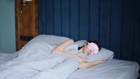 woman in a pink eye mask lies under a blanket in a bed and suffers from insomnia