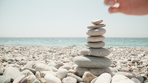Close-up, a woman makes a cairn. Handmade stone tower on the seashore. A stack of balanced pebbles on the beach. Against the backdrop of the sea
