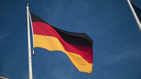 Slow motion of German flag waving in the wind. Flying black, red, yellow flag on flagpole against blue sky in Germany, Berlin. Background banner video. Symbol of German people and nation. FullHD.