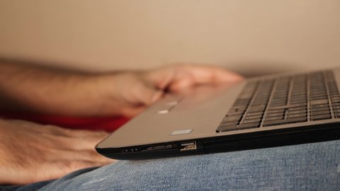 Close-up of a man watching an adult video on a laptop and stroking his genitals with his hand under his jeans