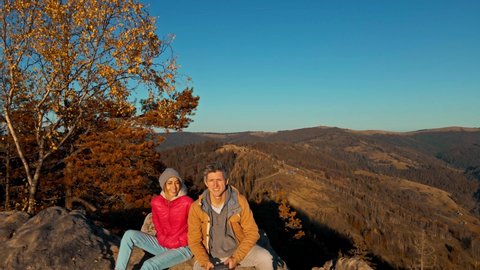 aerial drone selfie happy couple hikers sitting on top of cliff. man and woman travelers enjoying great view in Carpathian mountains, Ukraine. happy girl and man enjoys landscape together at sunset.