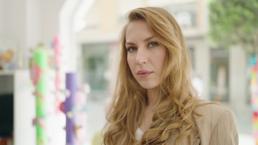 Young blonde woman shop assistant smiling confident standing with arms crossed gesture at clothing store