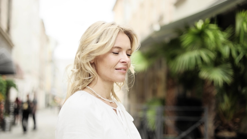 Portrait of attractive middle aged woman in white dress on the city street. Happy relaxed lady looking at the camera on the city centre enjoying. Royalty-Free Stock Footage #1091174831