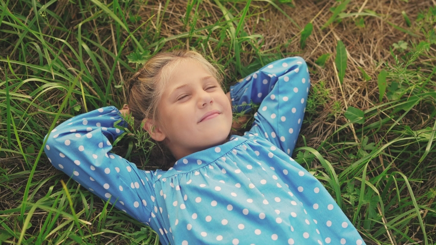 little girl child lies on the grass in the park. happy family kid dream concept. baby girl in the park lies on her back looks at the sky portrait close-up. girl in fun nature smiling portrait