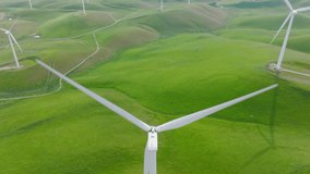 Renewable energy, sustainable development, environment friendly concept for copy background. 4K aerial view on summer day, USA Cinematic white wind turbine on beautiful perfect scenic green hill