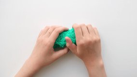 Hands Playing with textured slime with bubbles, stretching the gooey substance on white background. Female teen hand holding green shining slime toy, squeezing it to the sides. Top View. 4K video.
