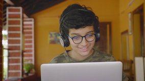 A young Indian Asian male student wearing headphones and eyeglasses talking, reading or interacting during online group class activity using a laptop. remote or distance education, technology concept