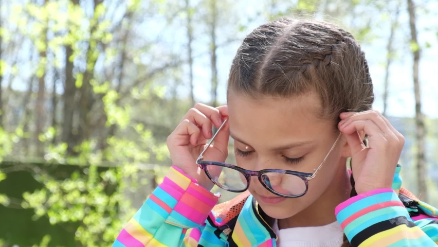Portrait of a cute teenage girl puts on eye glasses on the street, spring weather, cute child in trendy glasses | Shutterstock HD Video #1091185799