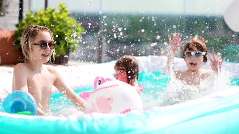 excited kids having fun, splashing water in inflatable pool at home patio, sunny summer activities