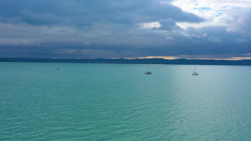 two boats sailing on the lake Balaton in the sunset with clouds in rainy weather, drone footage