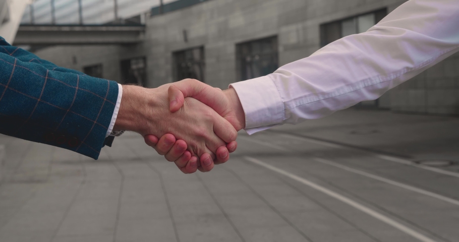 Close up of the hands of top managers in business suits, shake hands with each other, near building background, agree to a deal or say hello. Unrecognizable person.