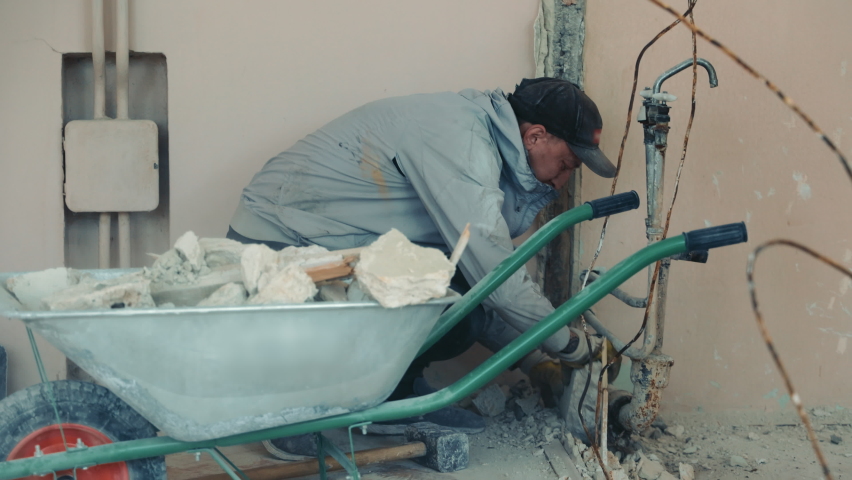 Reconstruction of the room and overhaul. Builders load construction debris with a shovel into a wheelbarrow. Royalty-Free Stock Footage #1091204849