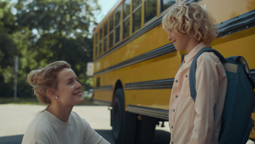 Cheerful mom giving son five at school transport close up. Smiling schoolboy get in yellow schoolbus. Little curly boy say goodbye mother before boarding. Young woman escorting child to classes.  Royalty-Free Stock Footage #1091205683