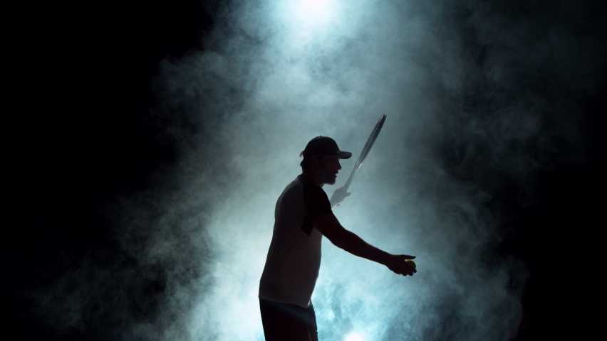 Super slow motion of tennis player silhouette hitting ball. Smoke effect around, black background. Speed ramp effect. Filmed on high speed cinema camera, 1000fps.