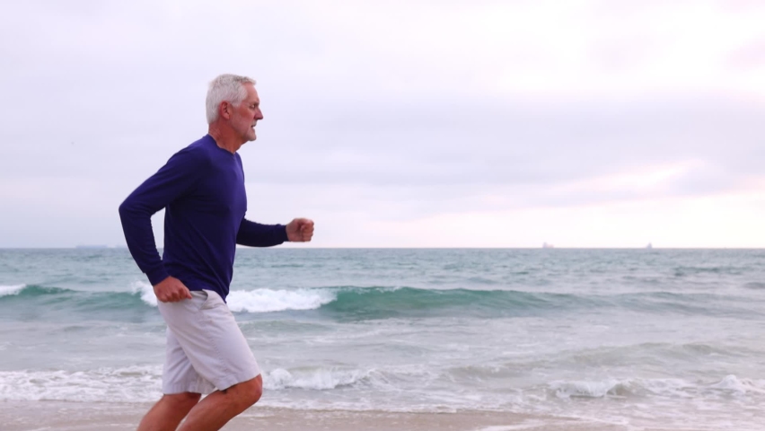 A mature 66 year old man jogging at the beach in Southern California. Slow Motion.