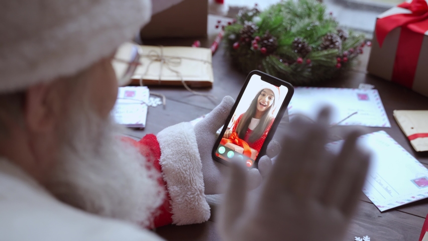 Over shoulder view of Santa Claus video calling kid girl on mobile phone greeting child by webcam talk open Christmas gift box in virtual online chat meeting using smartphone sit at table on xmas. | Shutterstock HD Video #1091209371