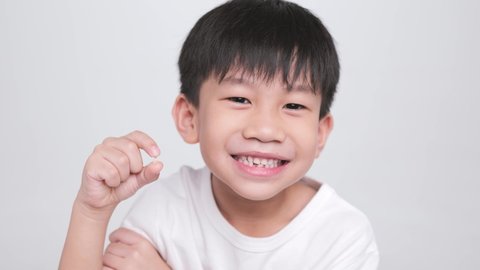 Asian kid holding the first fallen baby milk teeth while the second tooth loses and bends in his mouth. A happy boy proudly smiles at his dental care.